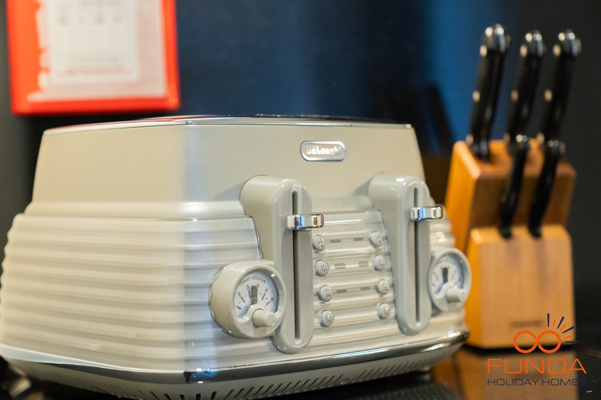 A vintage toaster with a dial for toast color, placed on a table with a knife block in the background.