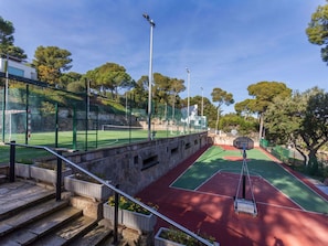 Una cancha de tenis con red, rodeada por una valla verde, y una escalera que baja hacia la cancha.