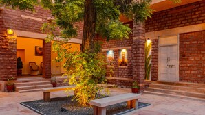 Un patio con un árbol, bancos y un edificio de ladrillo con una puerta y escalones.