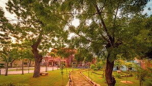 Un sendero atraviesa un jardín ajardinado con árboles y un edificio al fondo.