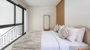 Una habitación de hotel moderna con un ventanal grande, una cama con ropa de cama blanca, una alfombra a rayas y una mesita de noche de madera.