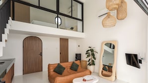 Una sala de estar moderna con un sofá, una mesa de centro, un espejo grande y una escalera que lleva a un nivel superior.