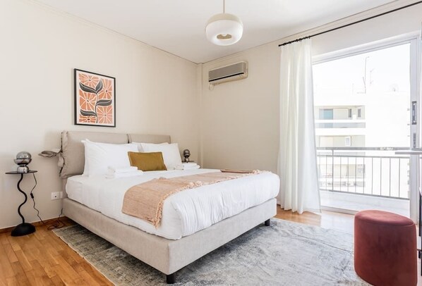 A bedroom with a bed, a bedside table, a floor lamp, a wall-mounted air conditioner, and a window with curtains.