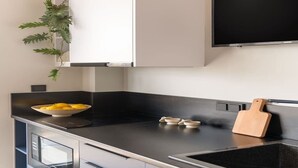 A modern kitchen with a black countertop, a bowl of lemons, a cutting board, and a potted plant. - Exceptional Living Loft 801 (Athina)