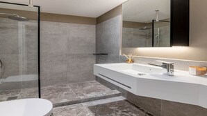 A modern bathroom with a glass shower enclosure, a white sink with a mirror above, and a large mirror on the wall. - Exceptional Living Loft 801 (Athina)