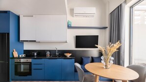 A modern kitchen with blue cabinets, a black stove, and a white wall-mounted air conditioner. - Exceptional Living Loft 704 (Athina)