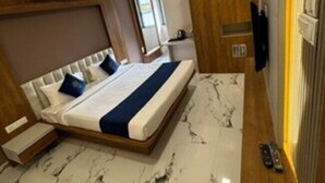 A modern hotel room with a large bed, marble flooring, wooden paneling, a TV, and an air conditioning unit.