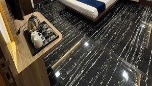 A modern hotel room with a bed, a desk with a kettle, a coffee maker, and a small table.