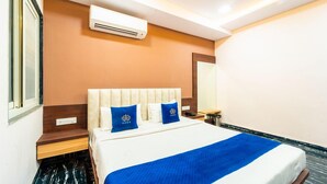 A hotel room with a bed, a nightstand, a mirror, and an air conditioning unit.