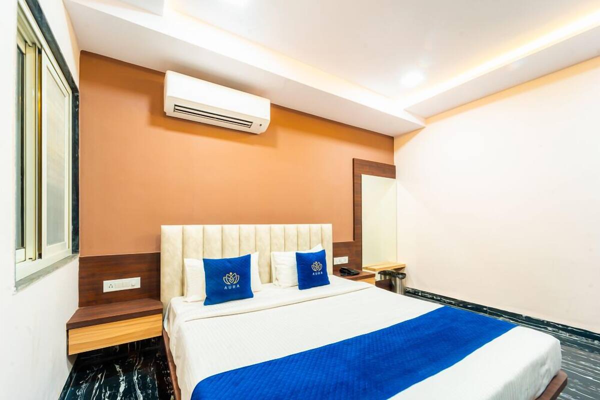 A hotel room with a bed, a nightstand, a mirror, and an air conditioning unit.