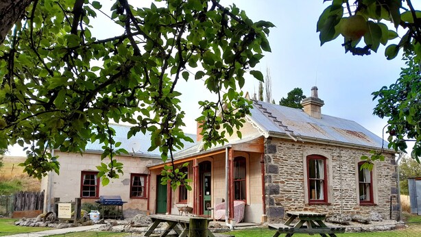 A stone cottage with a porch, two picnic tables, and a fenced yard. - Tregonning Cottage Waipiata (Waipiata)