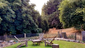 An outdoor area with a wooden bench, a stone wall, and a fenced area with trees and grass. - Tregonning Cottage Waipiata (Waipiata)