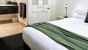A hotel room with a bed, a bedside table with a lamp, a mirror, a wardrobe, and a bathroom with a sink and towel rack. - Bendigo Holiday Accommodation (Bendigo)