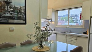 A modern kitchen with a glass dining table, chairs, and a vase with flowers. - Bendigo Holiday Accommodation (Bendigo)