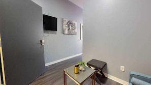 Enter a serene space with a door to your left, a table with a plant and decorative accent, and a comfortable bench with a cushion.
