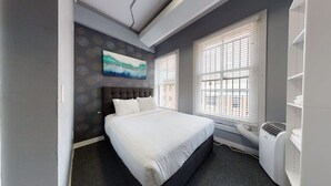 A modern hotel room with a large bed, a painting on the wall, and a window with blinds. - Downtown Crossing, Affordable Stay, Book Now! (Boston)