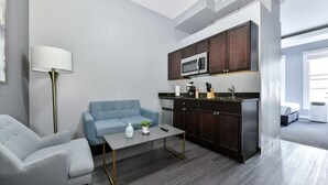 A modern living room with a sofa, coffee table, and a kitchen area with dark cabinets and a microwave. - Downtown Crossing, Affordable Stay, Book Now! (Boston)