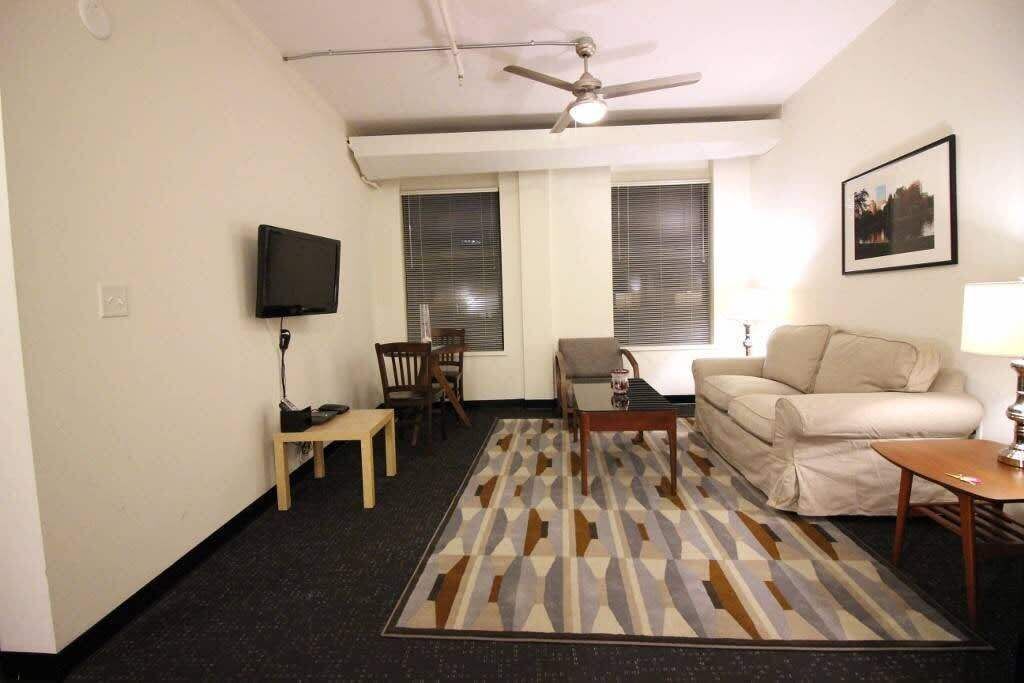 A living room with a ceiling fan, a television, a sofa, a coffee table, and a patterned rug.