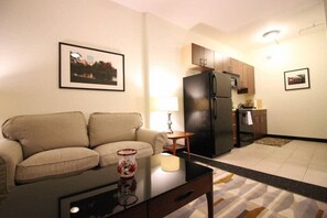 A living room with a sofa, a coffee table, and a kitchen area with cabinets and a refrigerator. - Perfect One Bedroom Stay In Downtown Boston! (Boston)