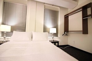 A hotel room with a large bed, two bedside tables with lamps, a window with blinds, and a wall-mounted TV. - Perfect One Bedroom Stay In Downtown Boston! (Boston)