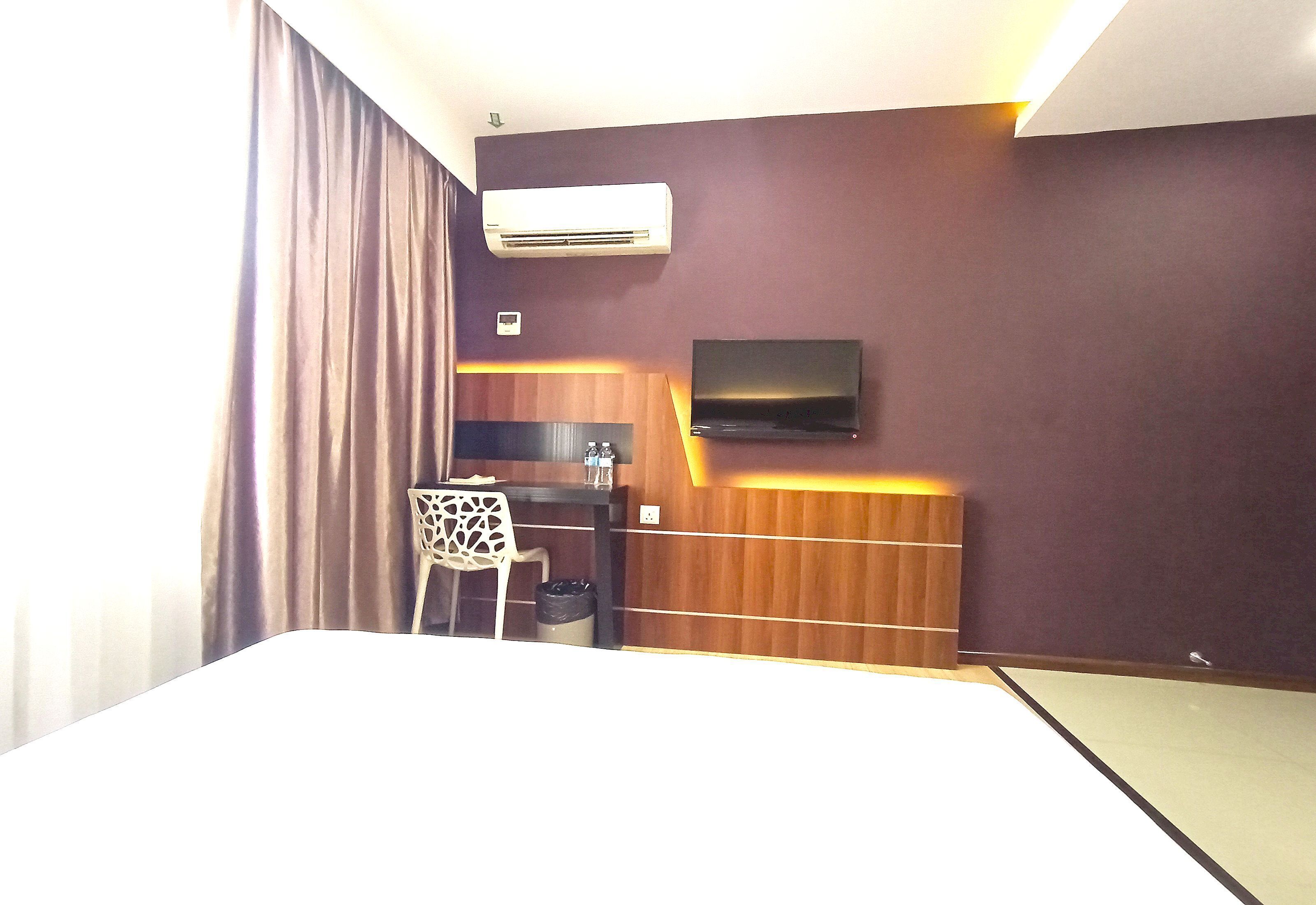 Een hotelkamer met een bed, een bureau, een stoel, een airconditioner en een aan de muur bevestigde televisie.