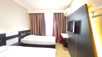 Een hotelkamer met twee bedden, een bureau, een televisie en gordijnen.