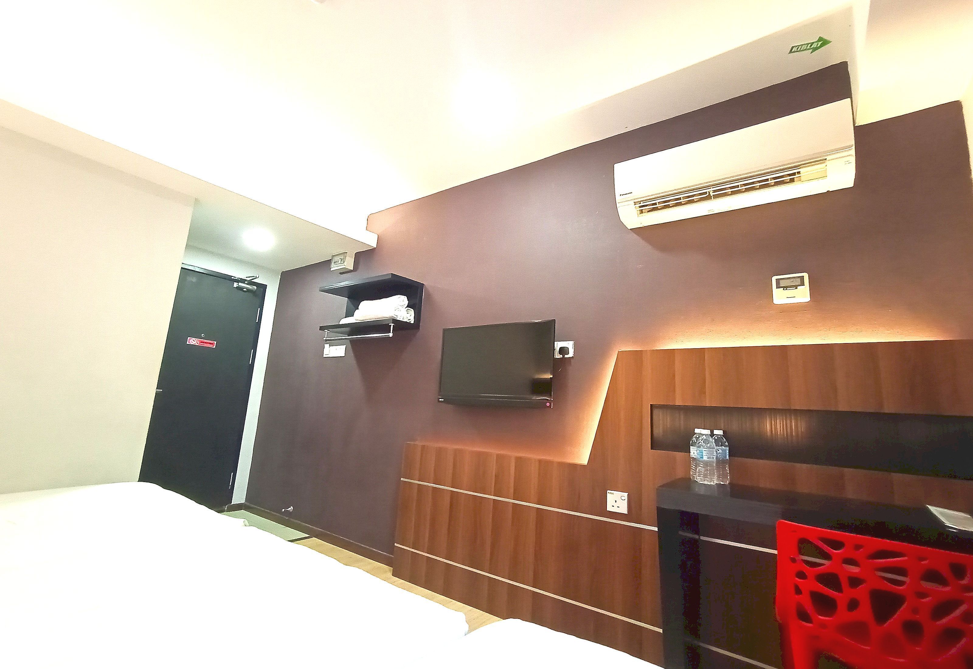 A hotel room with a bed, a desk with a chair, an air conditioning unit, and a wall-mounted shelf.