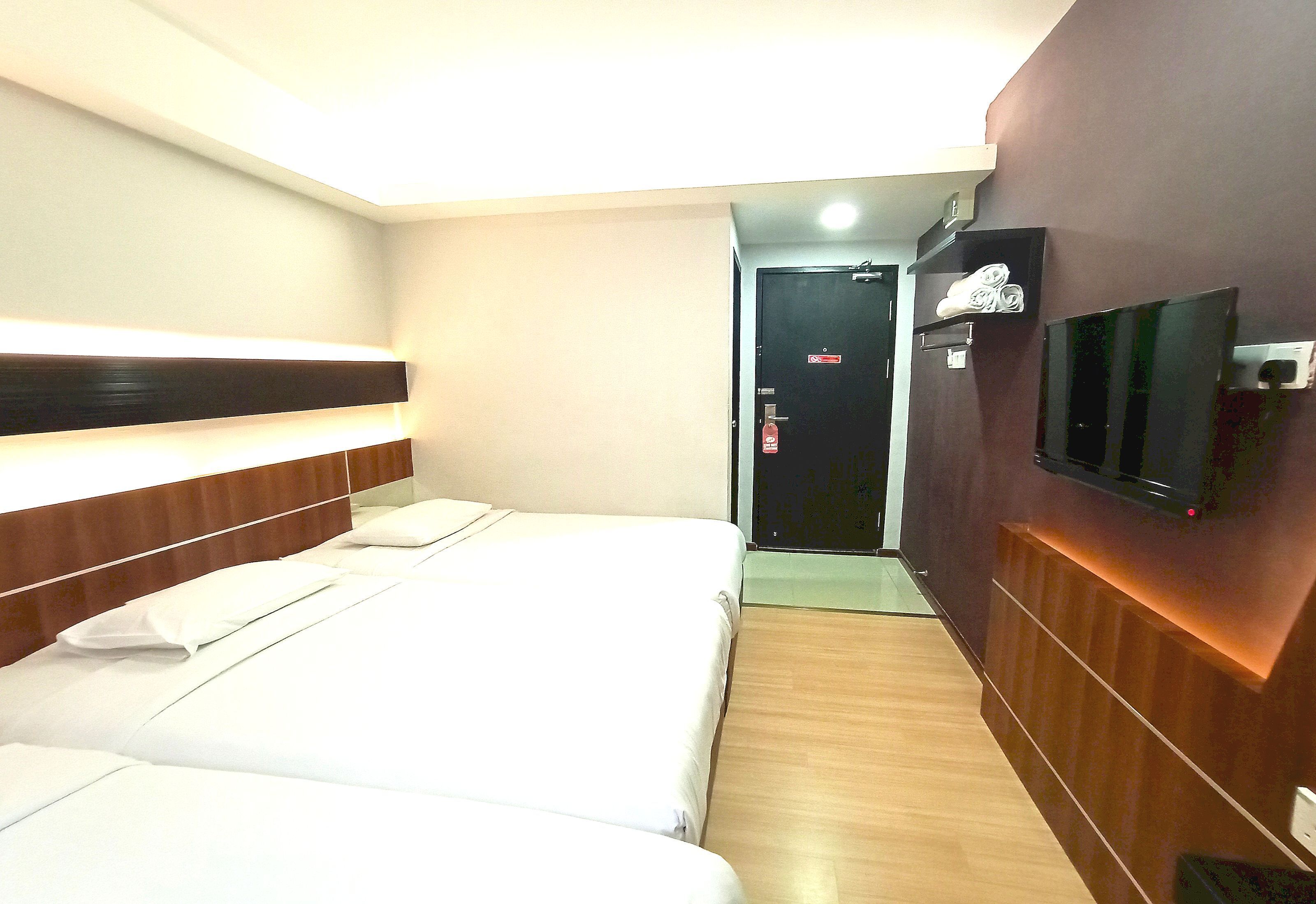 A hotel room with two beds, a TV mounted on the wall, and a door leading to the hallway.