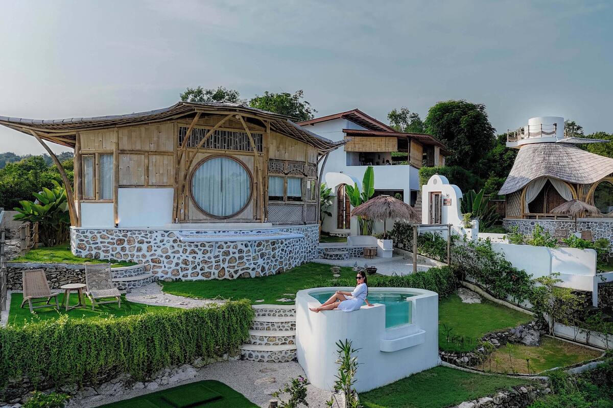 A villa with a large wooden structure, a swimming pool, and a thatched-roof building.
