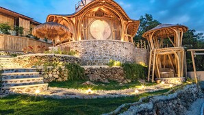 A rustic building with a stone facade, a large circular window, and a thatched roof structure. - Camanta Penida - Adult Only (Penida Island)
