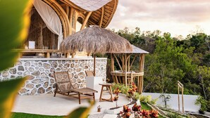 A rustic outdoor seating area with a stone wall, a thatched umbrella, and a wooden chair. - Camanta Penida - Adult Only (Penida Island)
