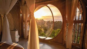 A room with a large circular window, a bed, and curtains. - Camanta Penida - Adult Only (Penida Island)