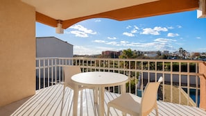 A balcony with a white table and chairs, a pool, and a view of buildings and palm trees.