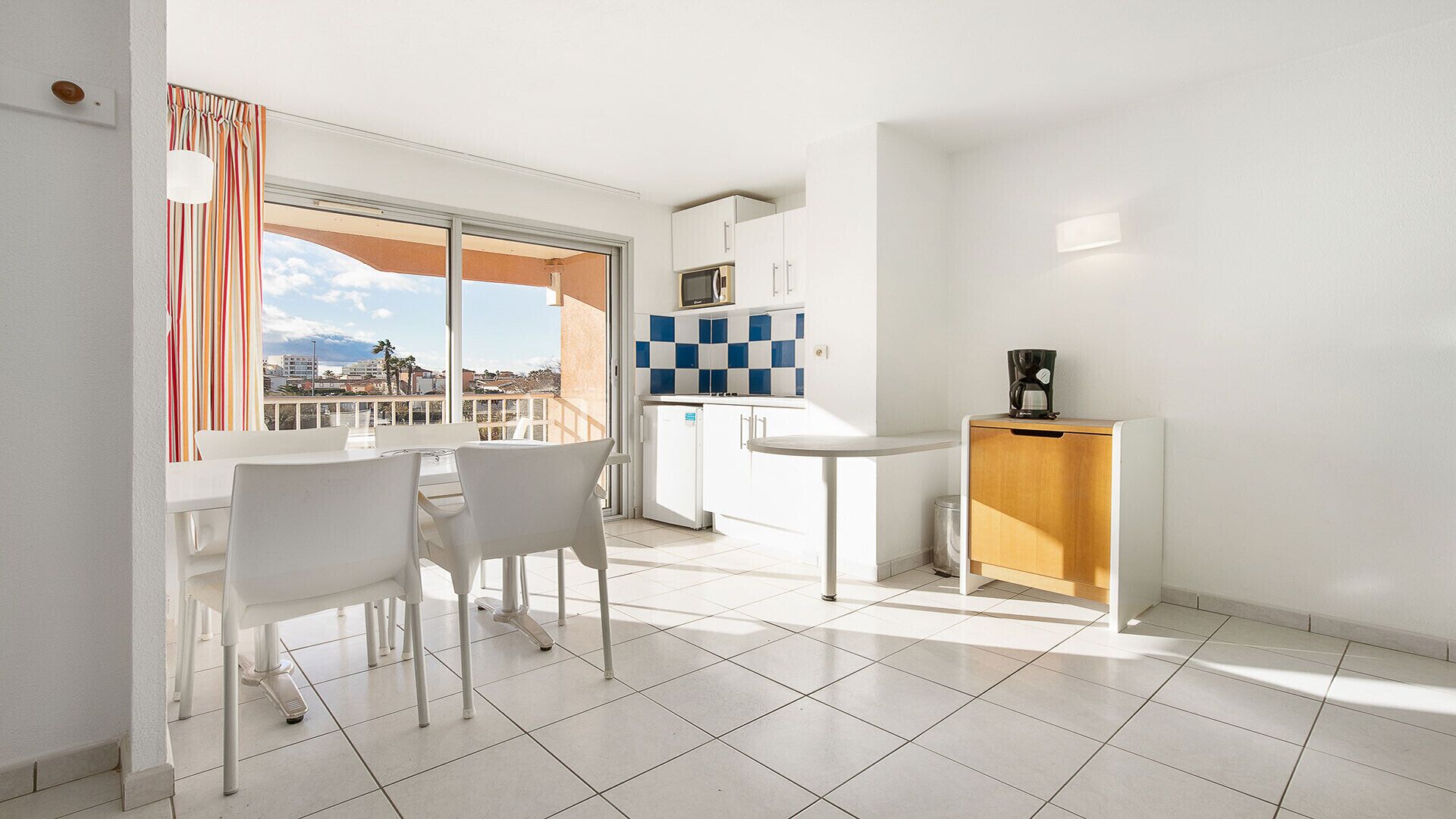 Een moderne kamer met balkon, een kitchenette en een zithoek met stoelen en een tafel.