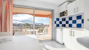 A balcony with a table and chairs, a sliding glass door, and a kitchen with a microwave and cabinets. - Apartment with a balcony, 300 meters from the beach (Agde)