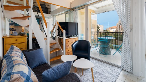 Un salon moderne avec un canapé, un téléviseur, un escalier et un balcon agrémenté d’une table et de chaises.