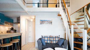 Un intérieur moderne comprenant un escalier, un coin cuisine et un espace salon avec un canapé et deux petites tables.