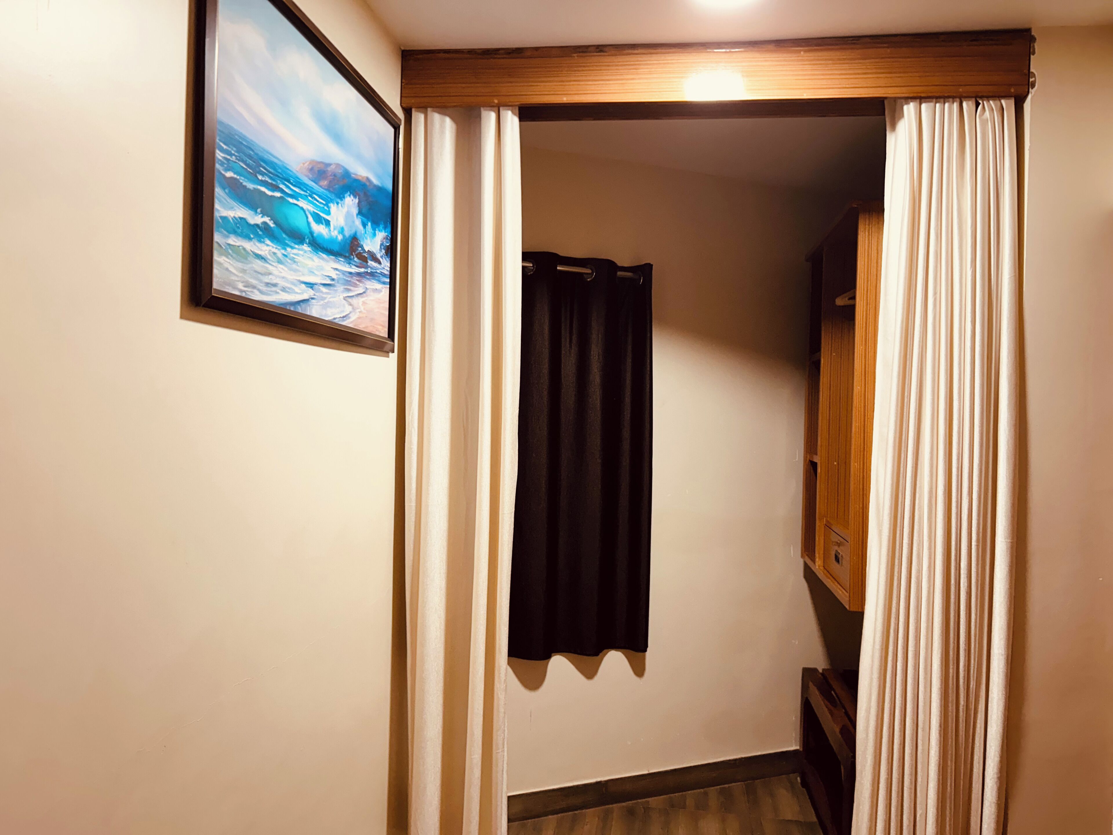 A narrow hallway with a wooden door frame, a black curtain, and a framed picture of a seascape on the wall.