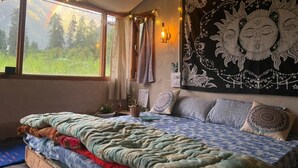 A bedroom with a large bed, a tapestry, and a view of greenery outside. - Zevibes Cafe & Homestay (Bhuntar)