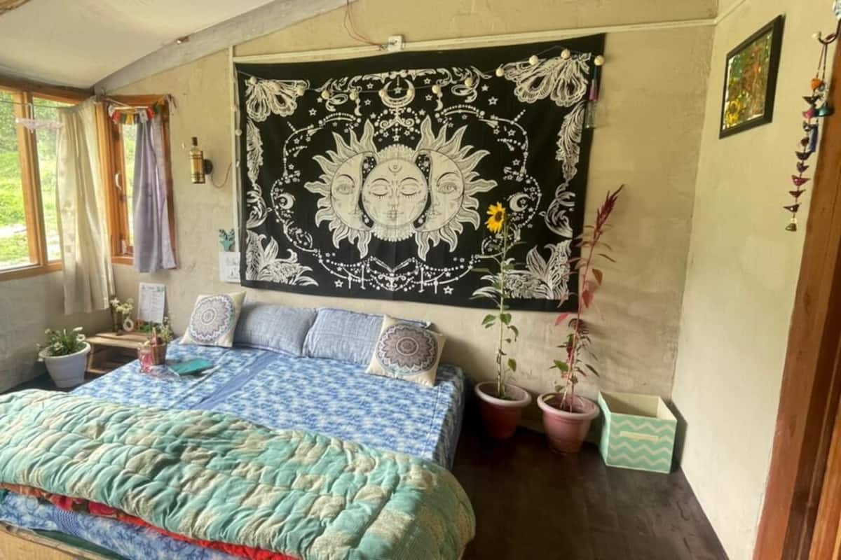 A bedroom with a bed, a tapestry, and potted plants.