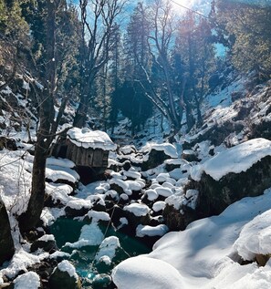 A snowy landscape with a wooden cabin and a river. - Zevibes Cafe & Homestay (Bhuntar)