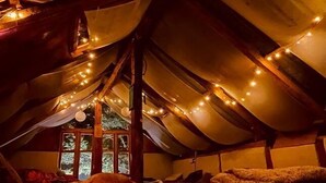 A cozy attic bedroom with a sloped ceiling, string lights, and a window with a view of greenery. - Zevibes Cafe & Homestay (Bhuntar)