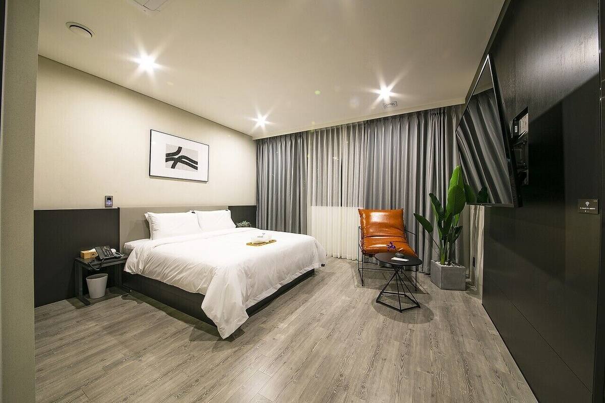 A modern hotel room with a bed, a desk, a chair, and a potted plant.
