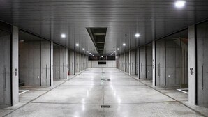 Un pasillo largo y vacío, con paredes de concreto y piso de baldosas, que conduce a una zona central con una escalera.