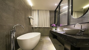Un baño moderno con una bañera independiente, un espejo grande y una encimera de mármol oscuro.