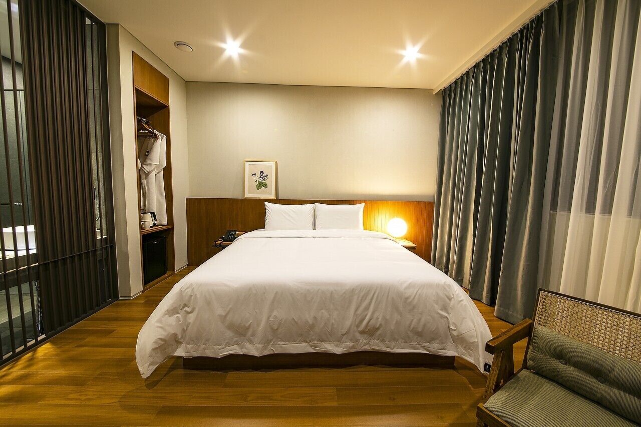 Habitación de hotel con una cama grande, suelo de madera, un armario y una mesita de noche con lámpara.