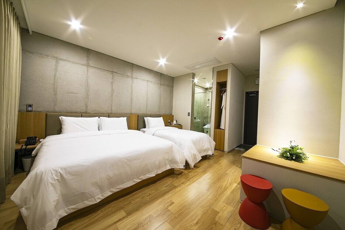 A hotel room with two beds, a wooden floor, a small desk with a plant, and a mirror.