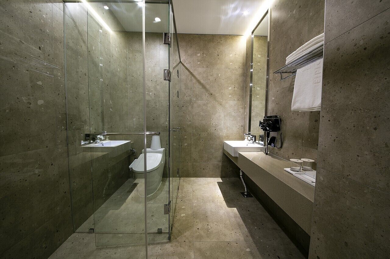 Un baño moderno con ducha envuelta en vidrio, inodoro y lavabo con barra para toallas.