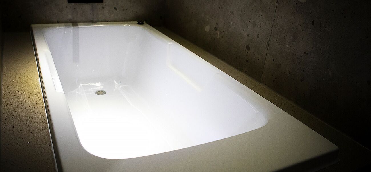 A modern, rectangular bathtub with a smooth, white surface and a single drain.