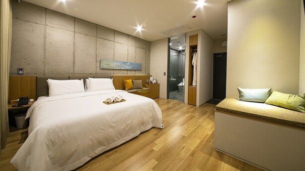 Habitación de hotel moderna con una cama grande, mesitas de noche, un área de descanso y vistas al baño.